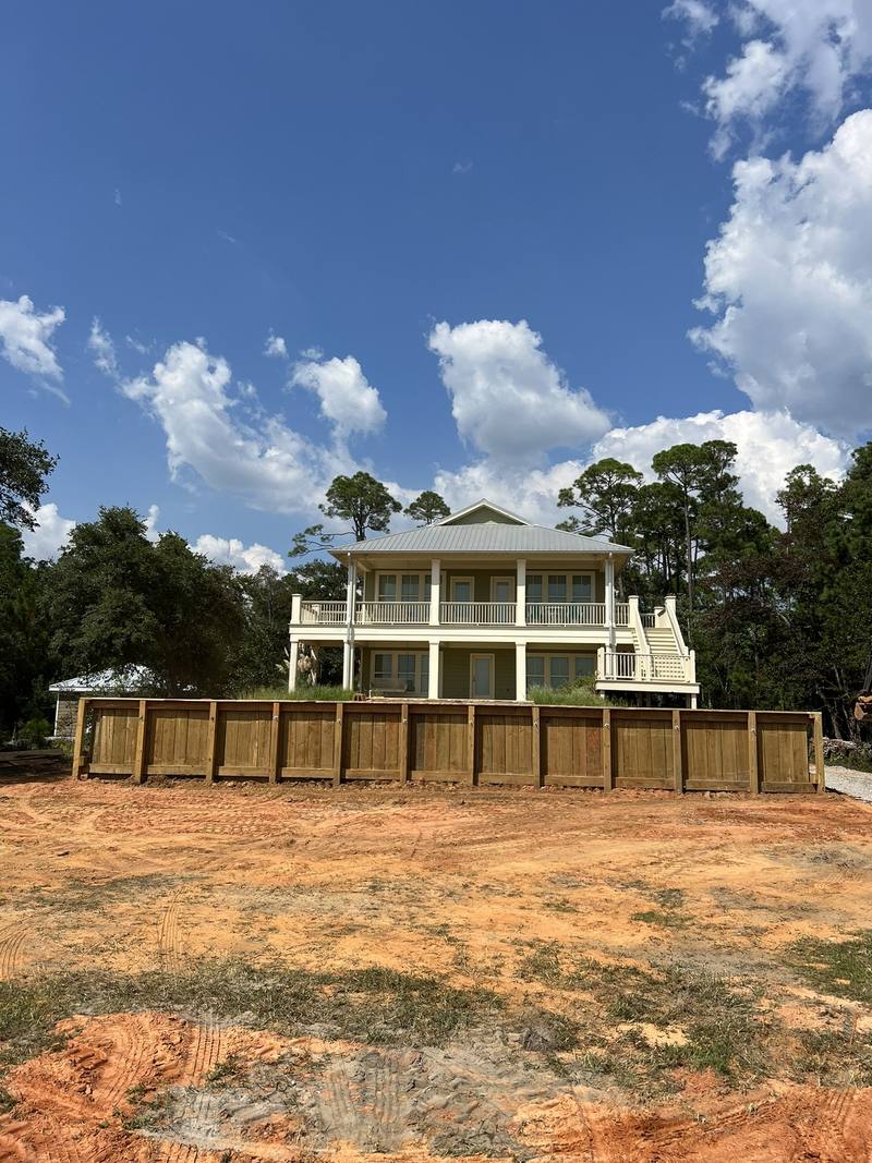Raised white coastal home behind a new wooden bulkhead and freshly graded yard