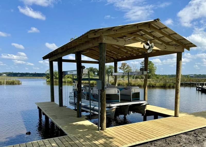 Open-sided boathouse with a pontoon boat on its lift and a wide wooden pier
