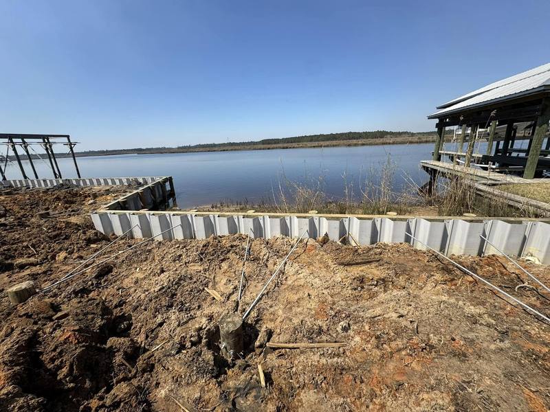 Vinyl bulkhead panels going in along a wide marsh, with an old boathouse beside it