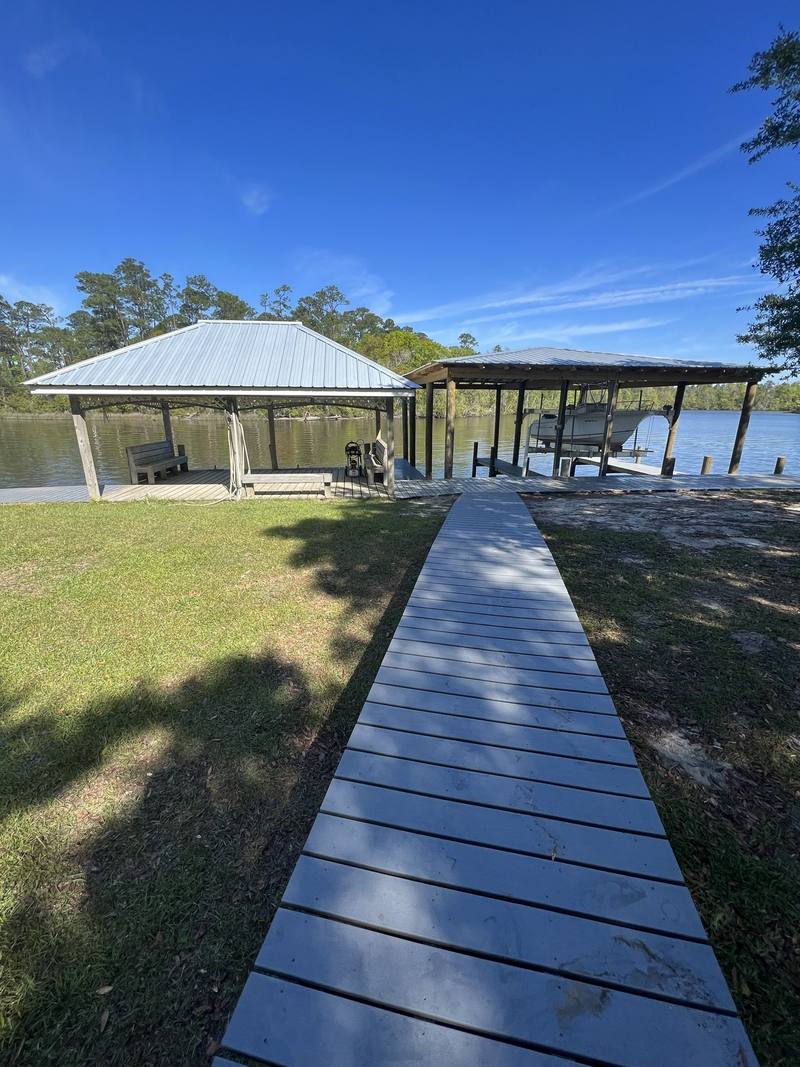 Wooden walkway across a lawn to a boathouse and a covered pavilion on the water
